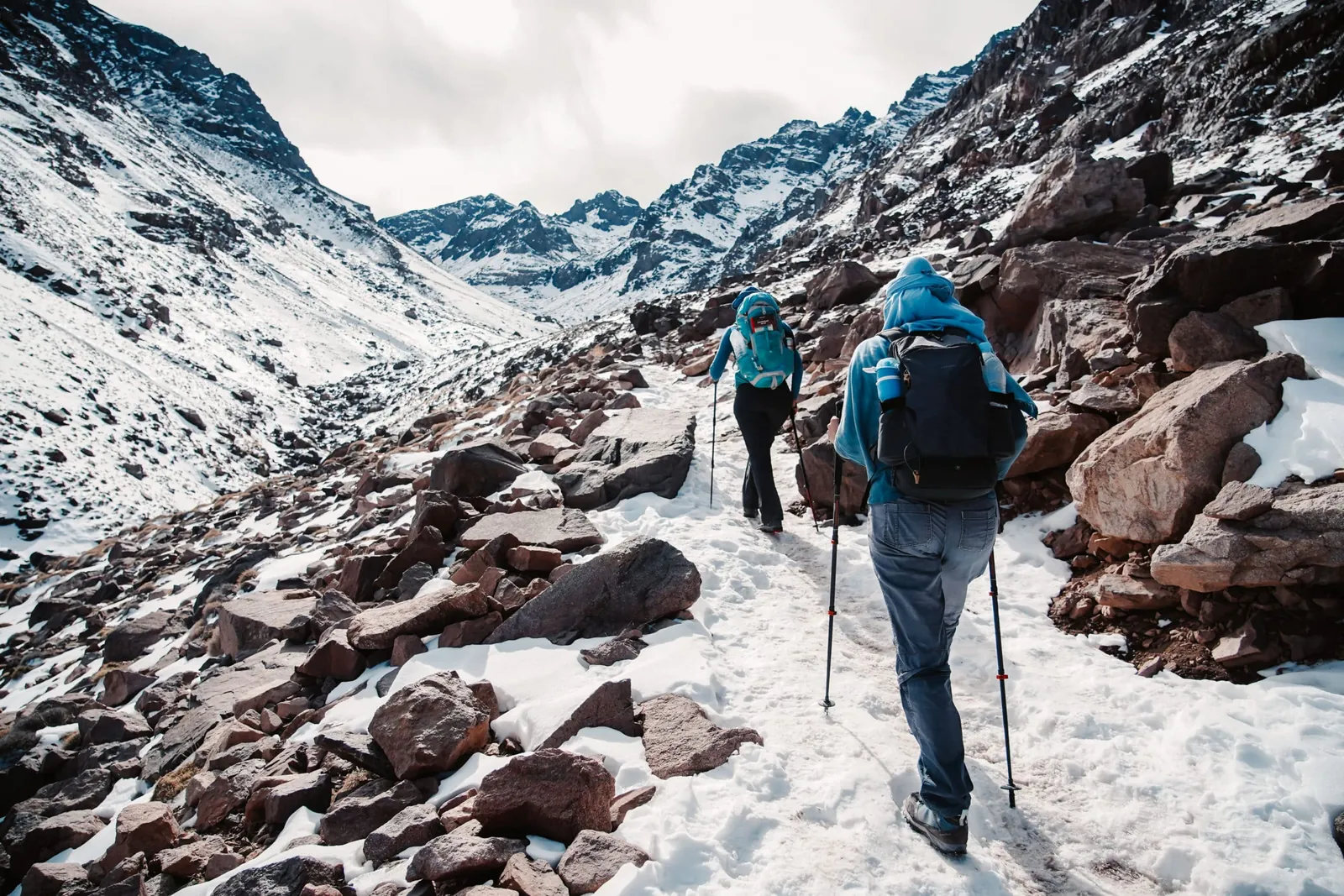 Hikers climbing a snowy trail toward Mount Toubkal in the High Atlas.